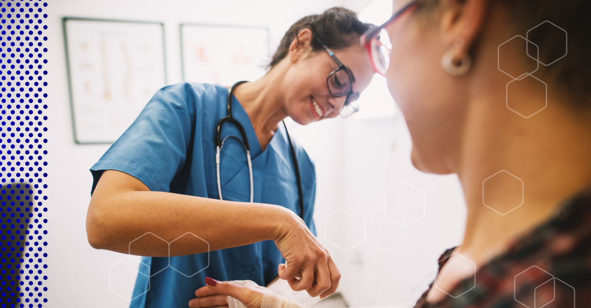 Stock image of smiling doctor wrapping her patient's hand in a bandage in a hospital room.