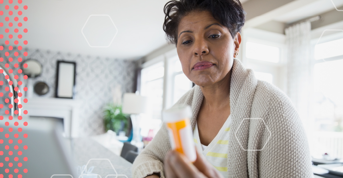 An older woman looks at a packer pill bottle in front of her computer.